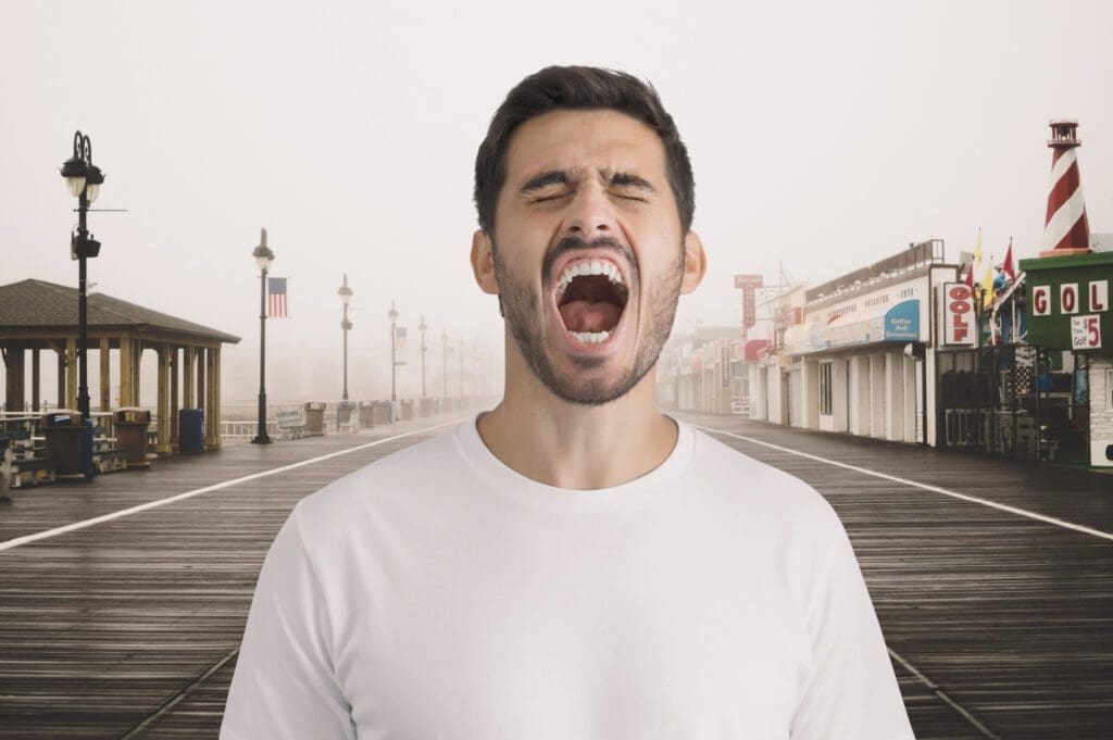 Un homme en chemise blanche se tient sur une promenade vide avec des boutiques et des lampadaires, la bouche grande ouverte comme s'il criait ou hurlait. Le ciel est couvert et l'arrière-plan est brumeux.