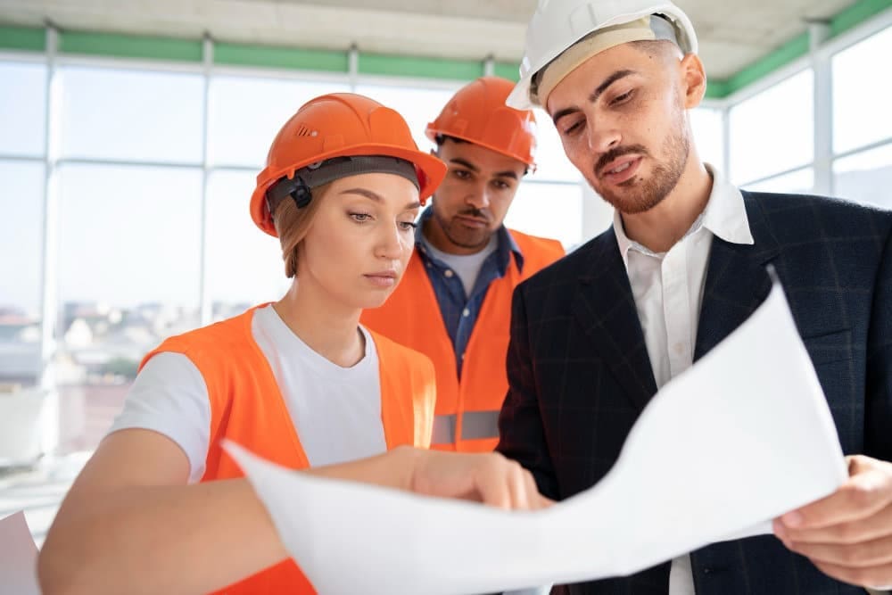 Trois professionnels du BTP discutent d'un plan sur un chantier, axés sur la prévention des risques.